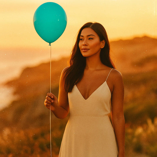 Woman holding a teal balloon against a sunset background