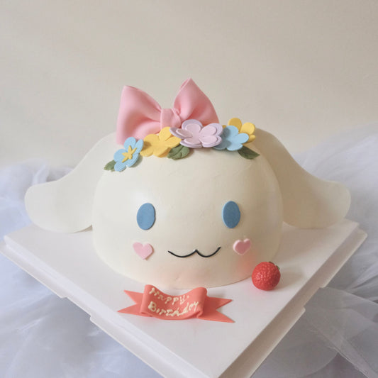 A decorated cake resembling a baby version of the Cinnamoroll character, with a cream-colored body, a pink bow, and floral accents on top.