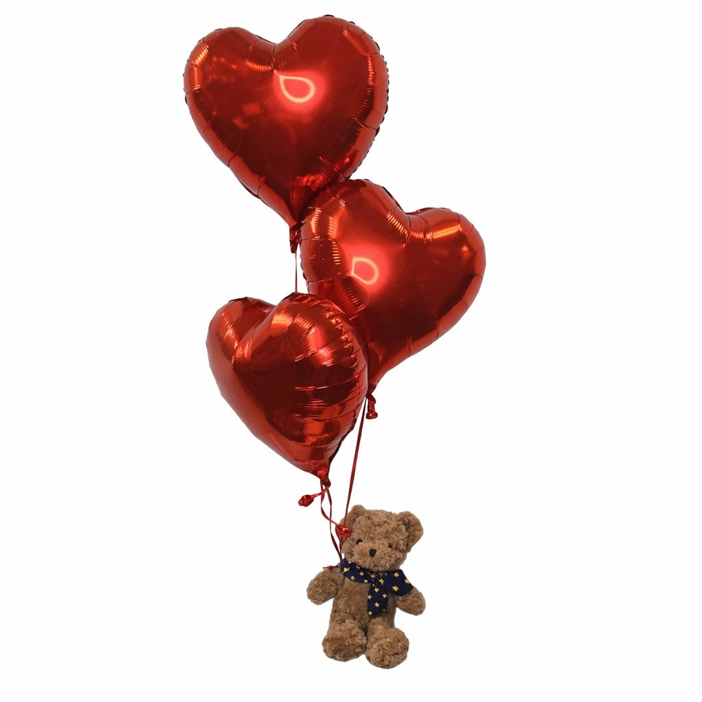 Three red heart-shaped balloons with a small teddy bear attached on a white background
