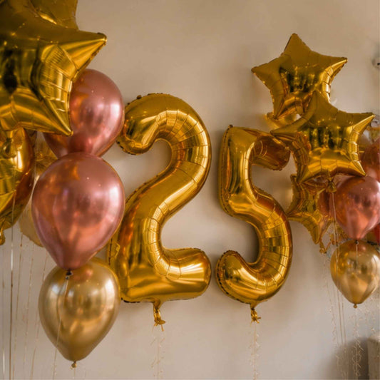 Gold foil number 25 balloons with matching gold and rose gold balloons, arranged against a plain beige wall.
