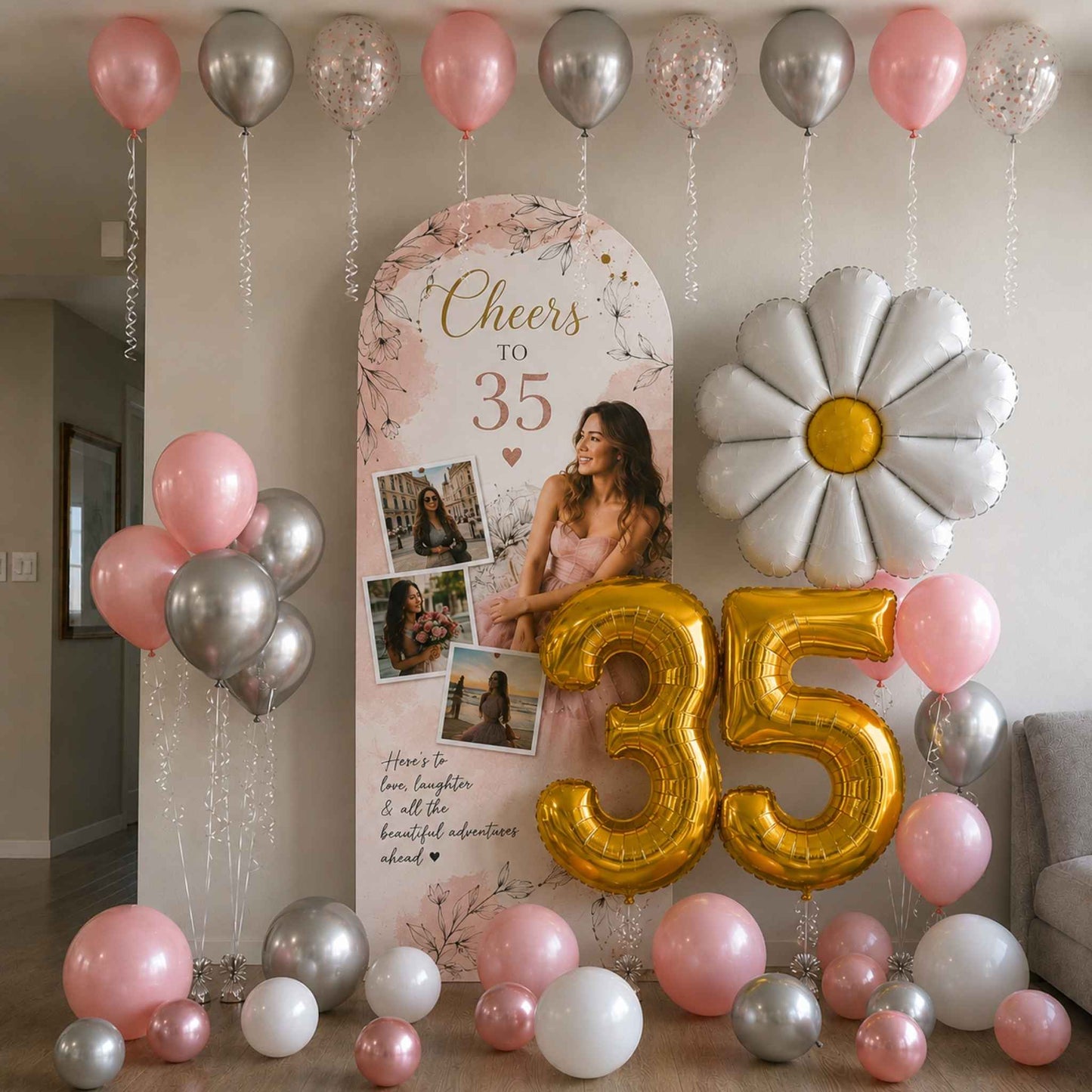 A decorated 35th birthday party backdrop featuring a large gold foil '35' balloon, a white daisy balloon, pink and silver balloons, a floral arch banner reading 'Cheers to 35,' and photo frames on a party backdrop stand in a living room.