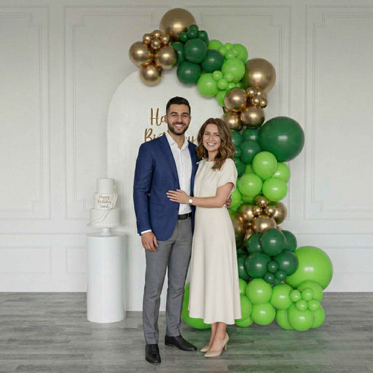 Man and woman posing in front of a balloon backdrop with green and gold balloons.