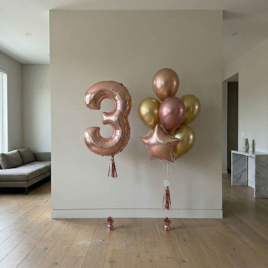 Rose gold number '3' balloon and cluster of balloons against a neutral wall.