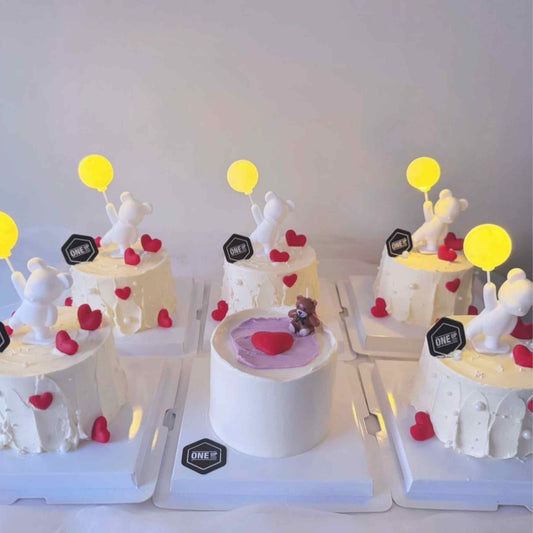 Small cakes with white figures, red hearts, and yellow balloons on a white background