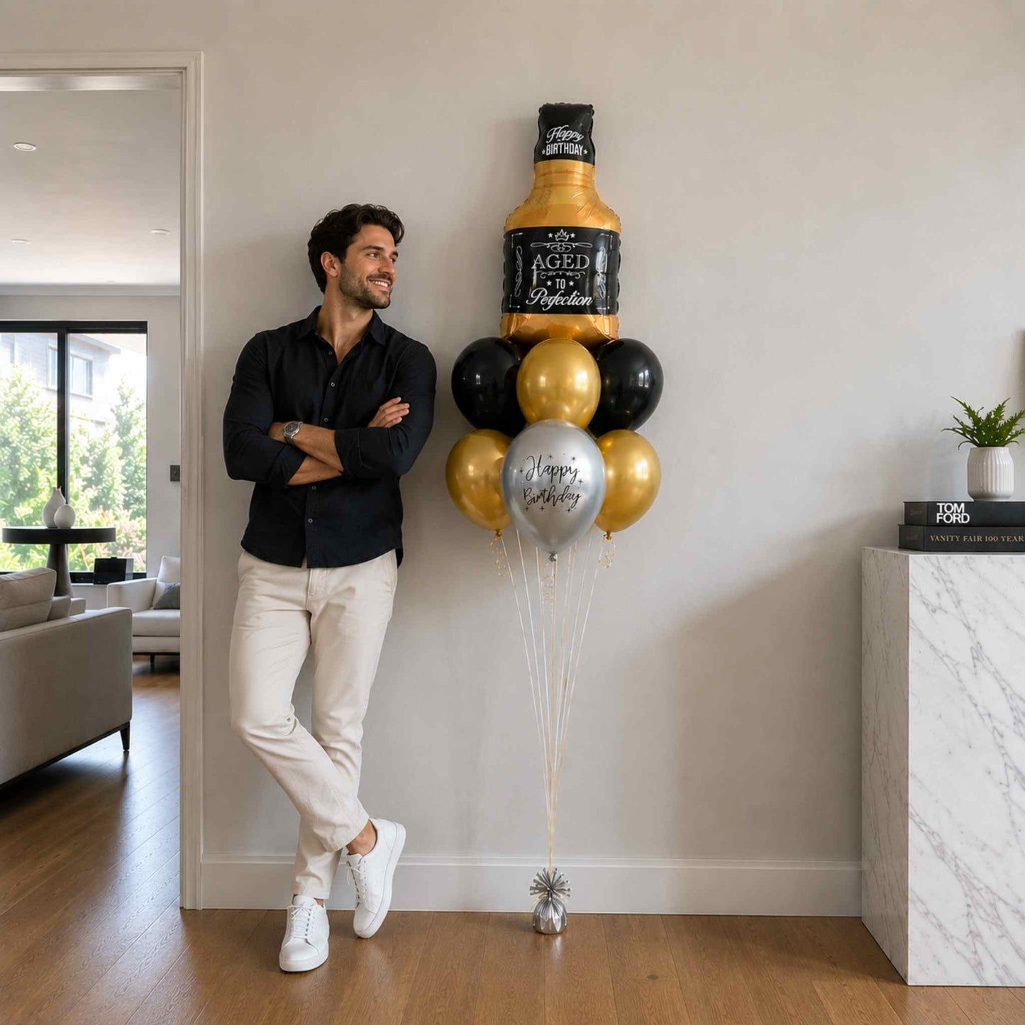Man standing next to a large bottle-shaped balloon with a bottle design in a living room.