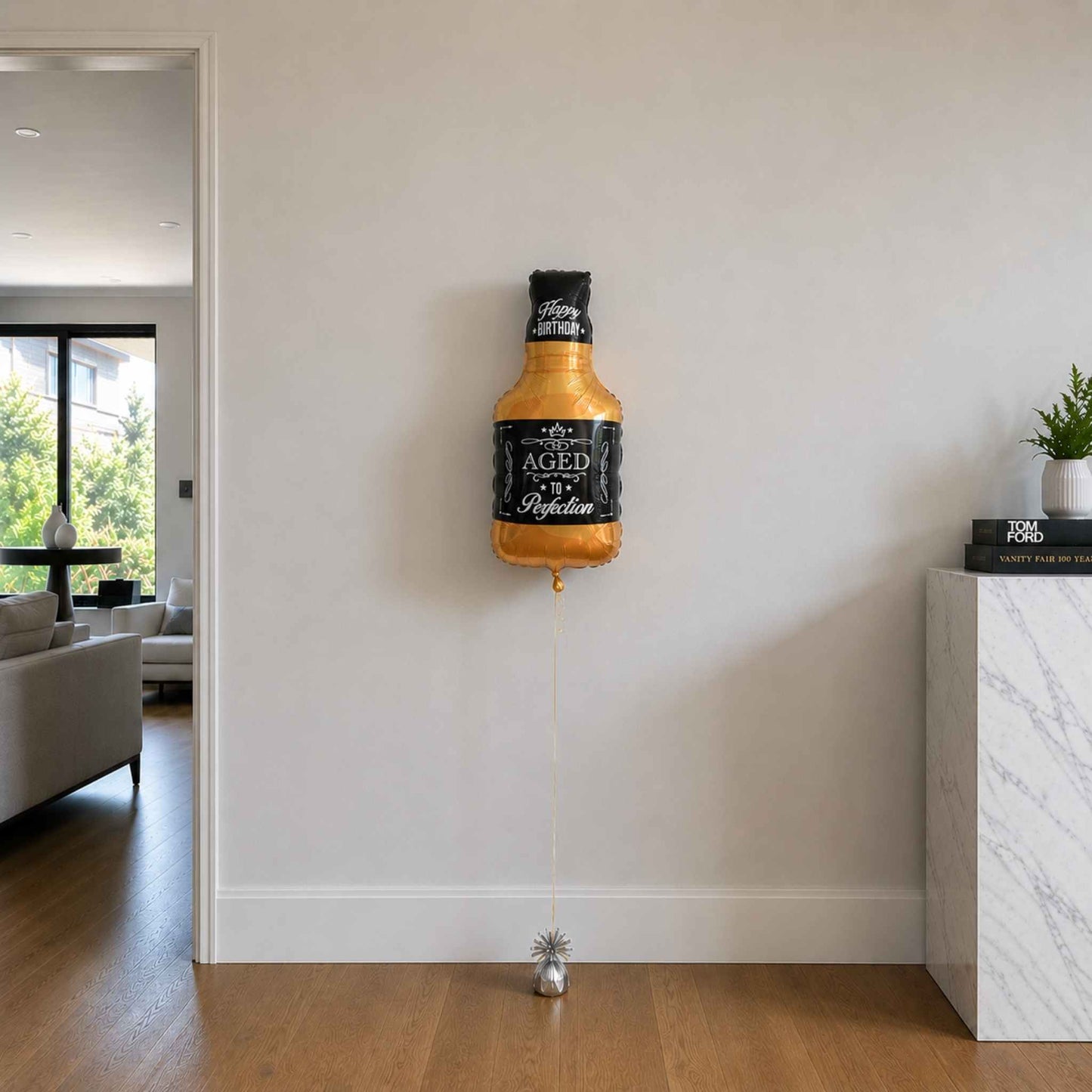 Bottle-shaped balloon with 'Aged to Perfection' text on a wall in a living room.