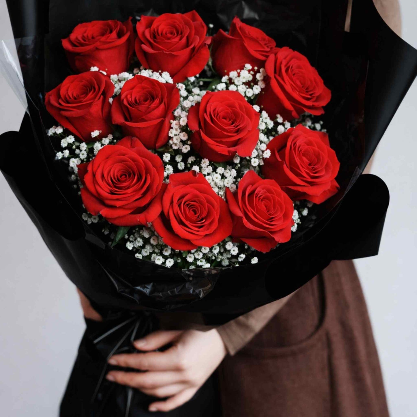Bouquet of red roses with a black wrap held by a person.