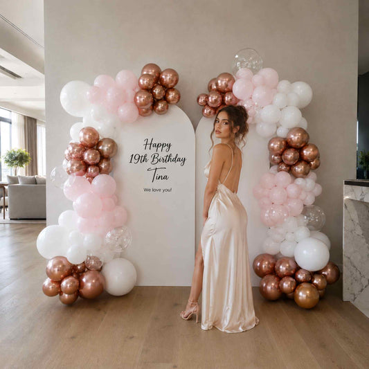 Woman in a satin dress standing between two balloon arches with 'Happy 19th Birthday Tina' text.