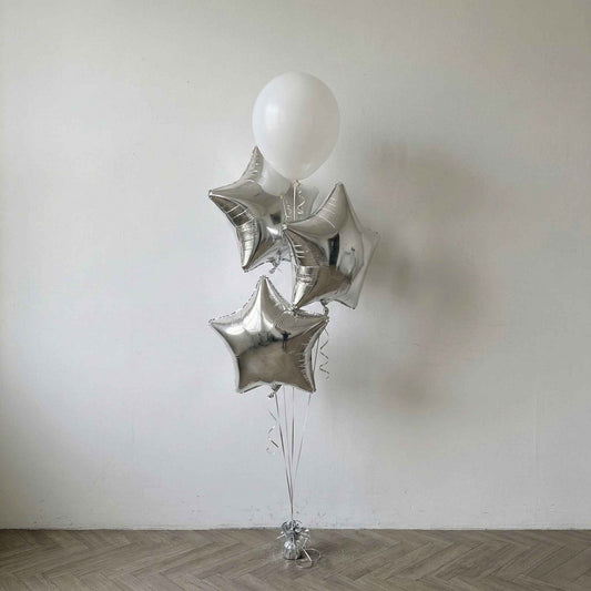 Silver star-shaped foil balloons with white latex tied together against a plain white wall.