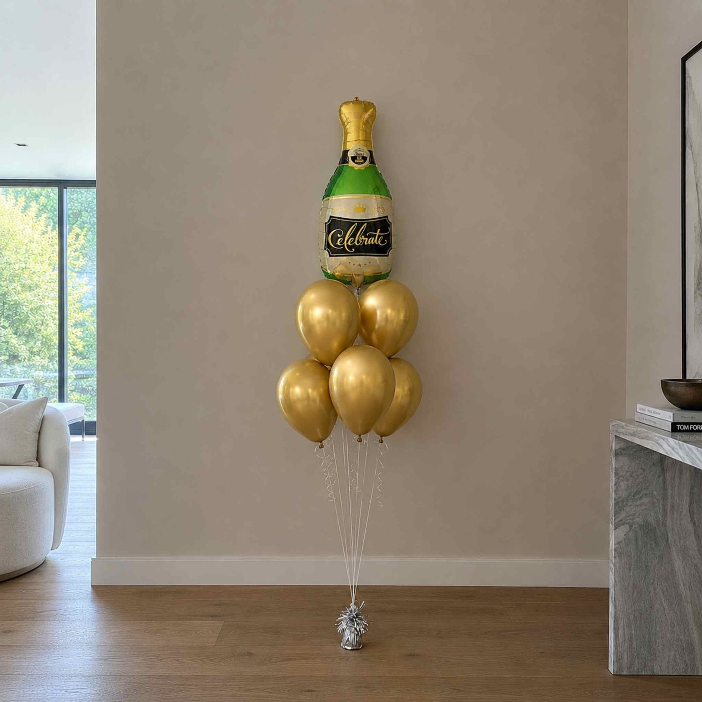 Gold champagne bottle balloon decoration against a beige wall in a living room.