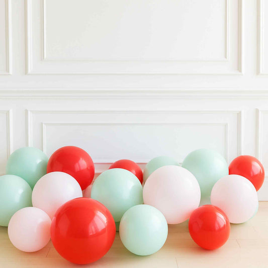 Colorful balloons in red, green, and white on a light wooden surface with a white paneled wall background.