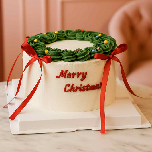 Christmas-themed cake with green icing wreath and red ribbons on a white stand.