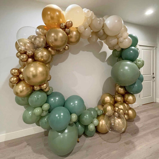 Balloon arch with gold, green, and white balloons in a room.