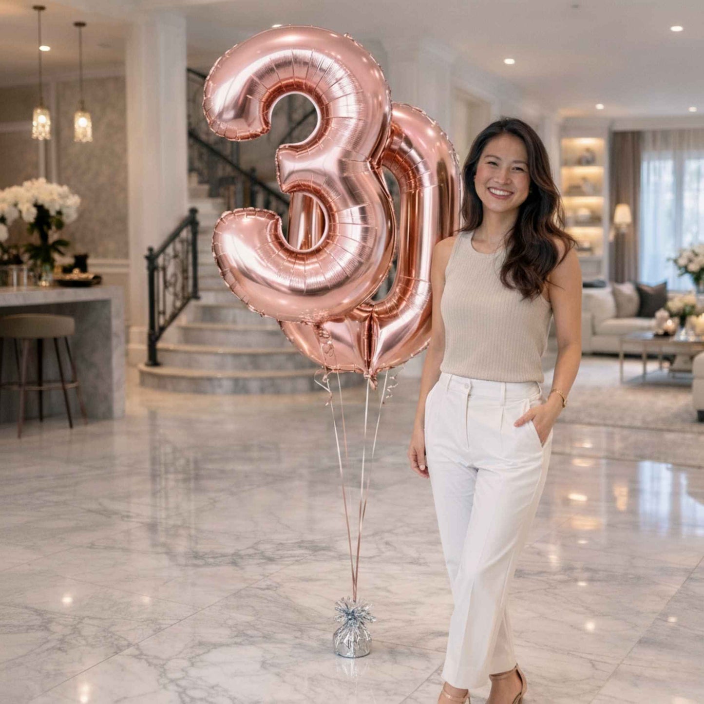 Woman poses by rose gold number 3 and 0 balloons in a modern home setting