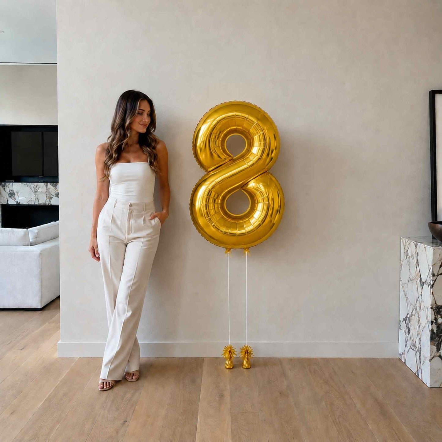 Woman standing next to a large gold number 8 balloon indoors.