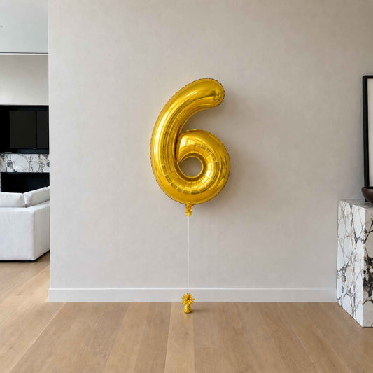 Gold number 6 balloon against a neutral wall in a room with modern decor.
