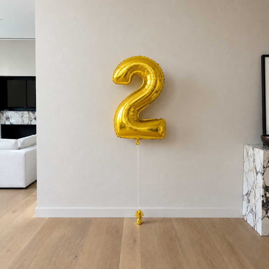 Gold number 2 balloon against a white wall in a modern living room.