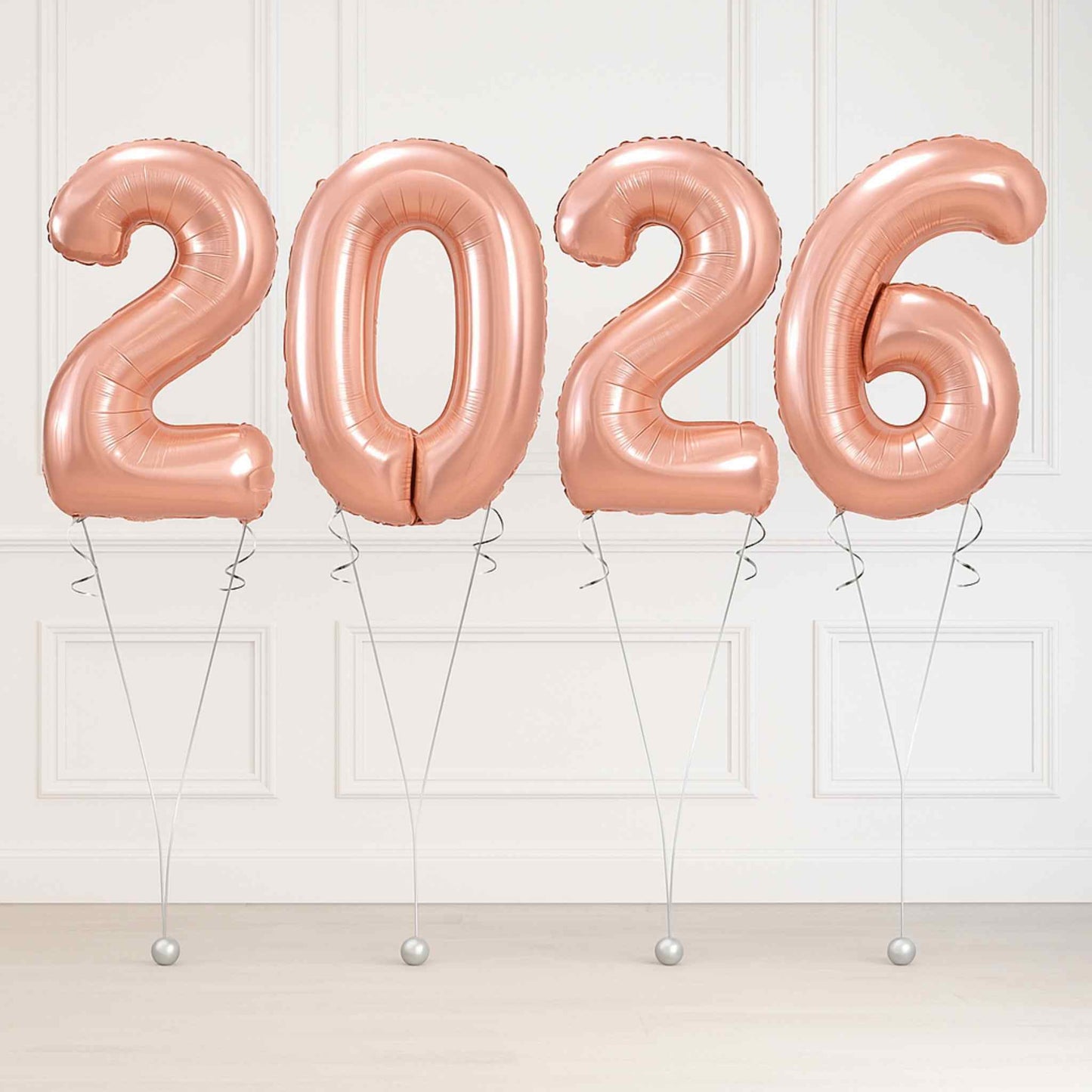 Rose gold '2026' balloons against a white wall.