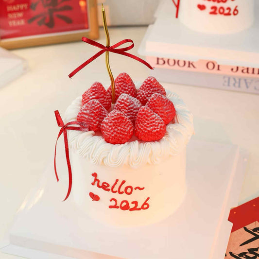 Small white cake with red berries and a red ribbon, featuring 'hello~ 2026' text, on a light background.