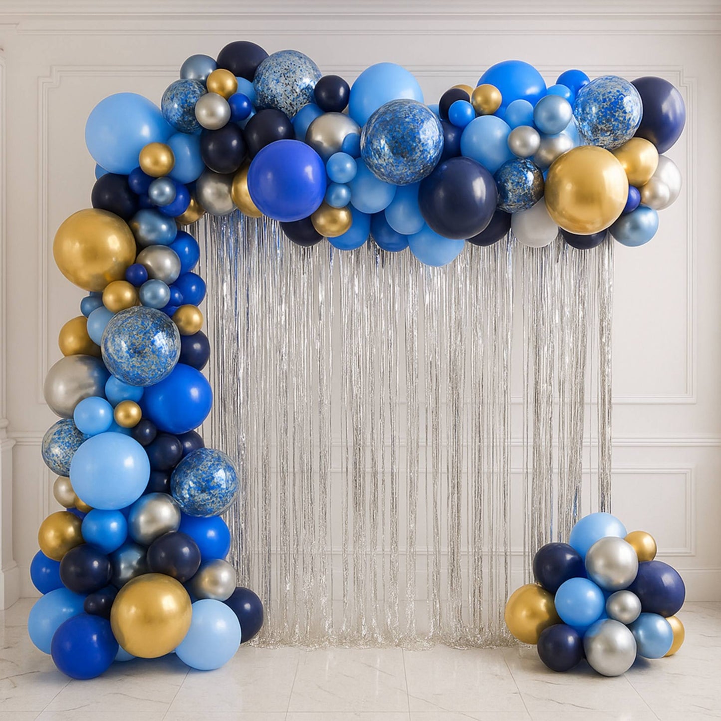 Balloon arch with blue, gold, and silver balloons against a textured wall.