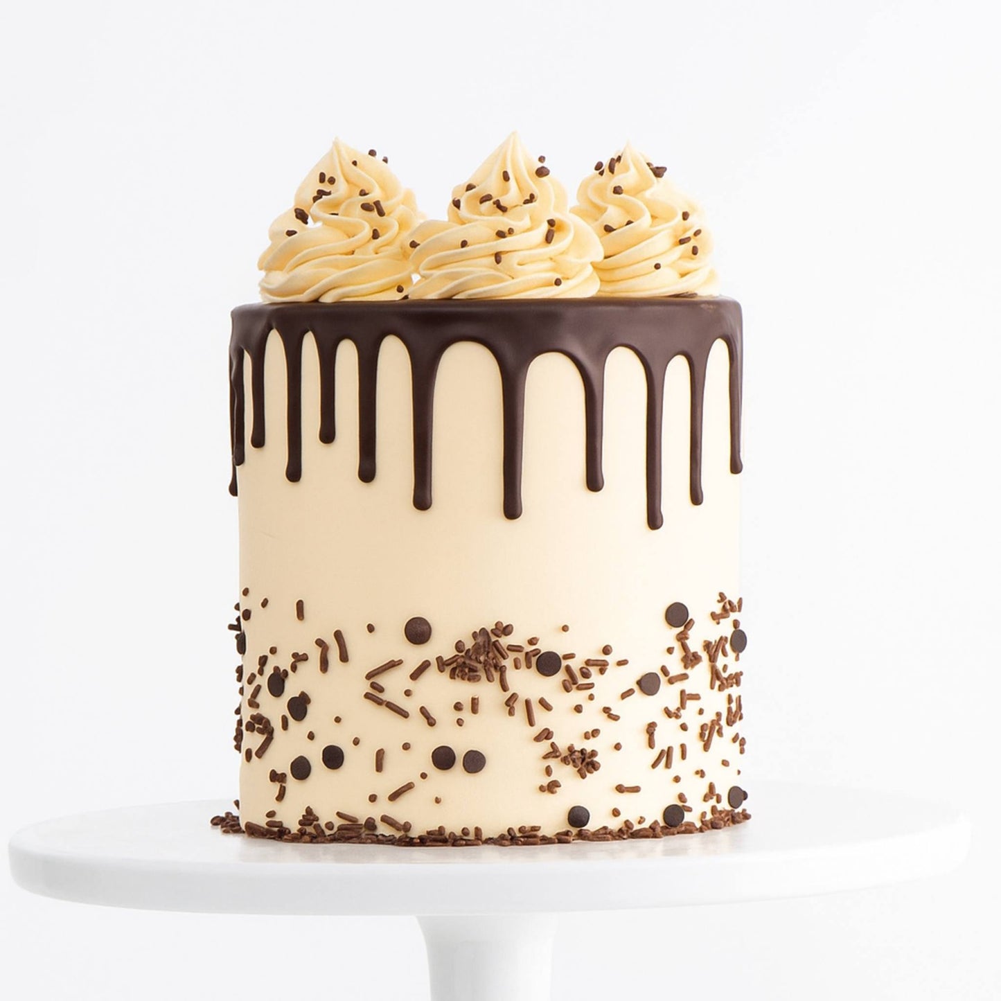 Chocolate drip cake with vanilla frosting and sprinkles on a white background