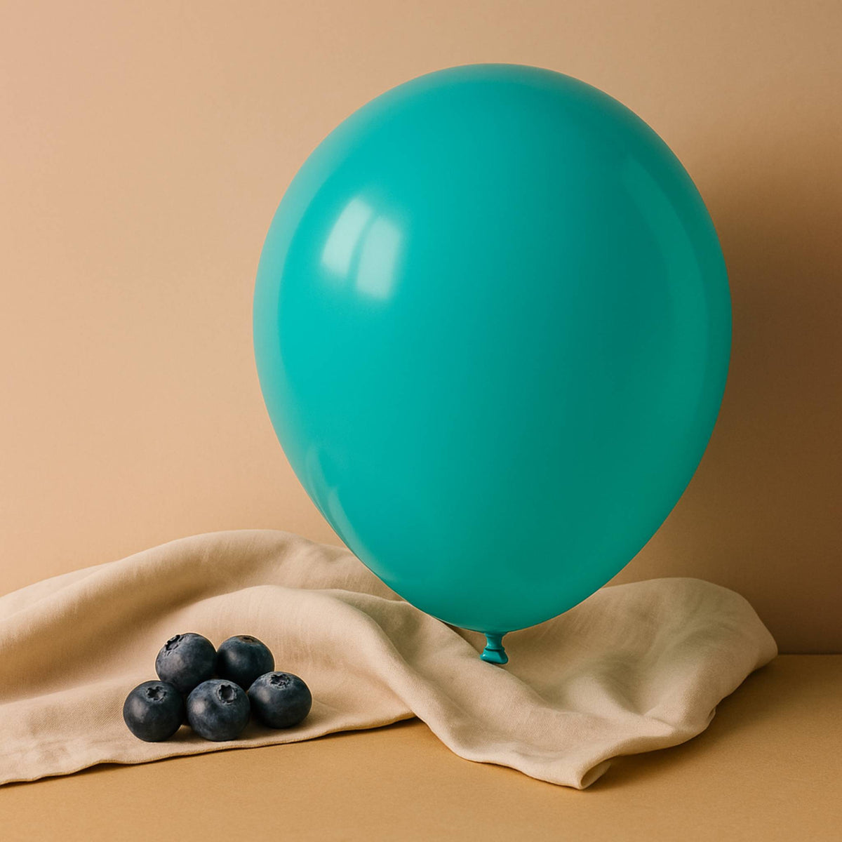 Turquoise 11 inch helium balloon on a beige cloth with blueberries against a beige background