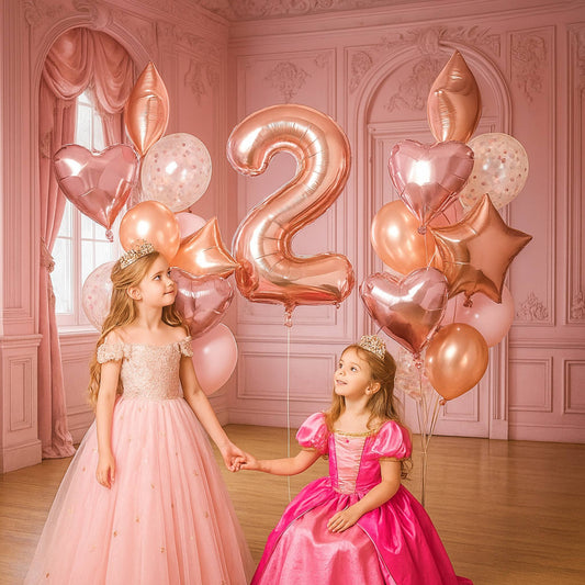 Two young girls in pink dresses holding hands with rose gold balloons shaped like numbers and heart shapes in a decorated room.