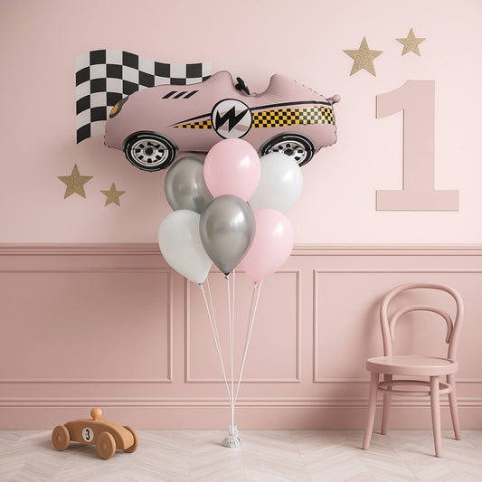 Pink car-shaped balloon with balloons in a room with a pink wall, chair, and small wooden toy car.