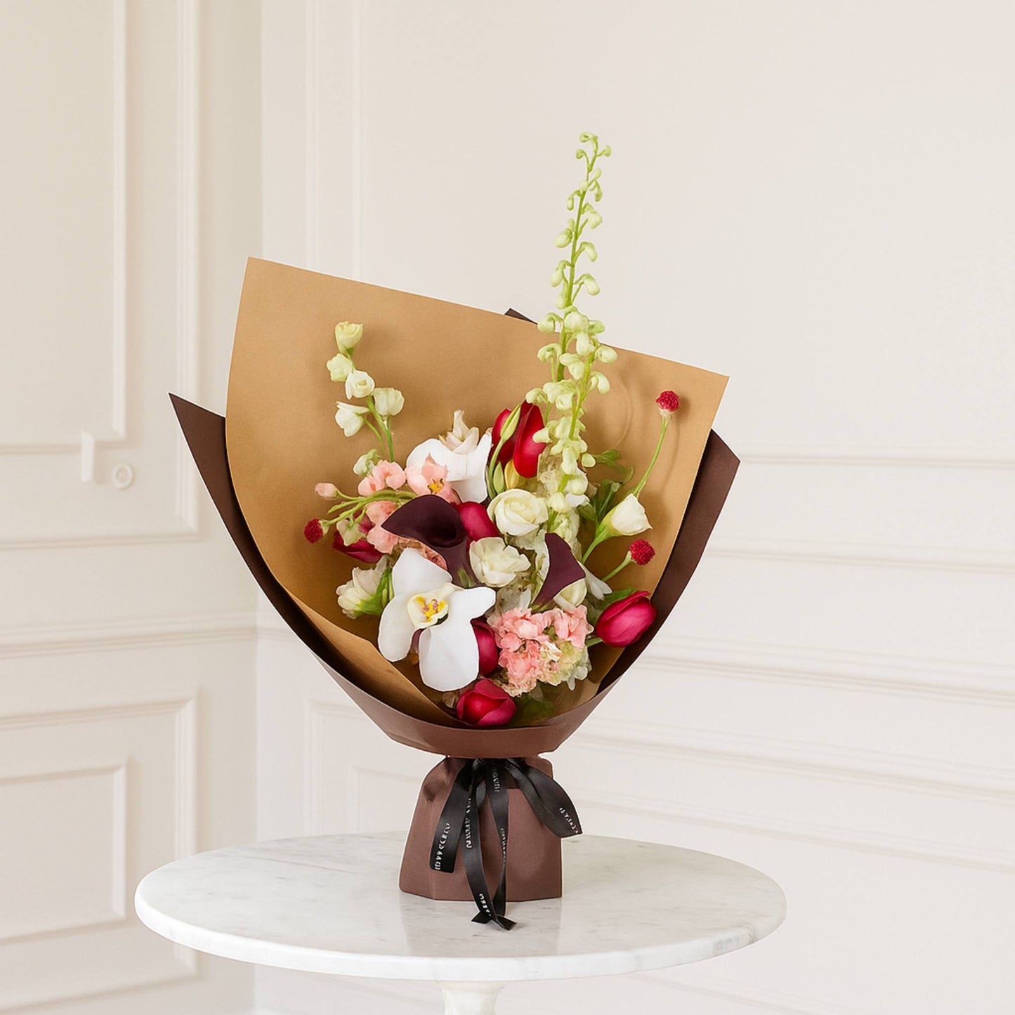 Bouquet of flowers wrapped in brown paper on a white pedestal against a light-colored wall.