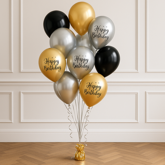 A bouquet of balloons arranged with a mix of gold, silver, and black colors, featuring 'Happy Birthday' text on some of the balloons, placed on a stand against a wall.