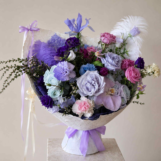 Bouquet of flowers with a white wrap and purple ribbon on a light background