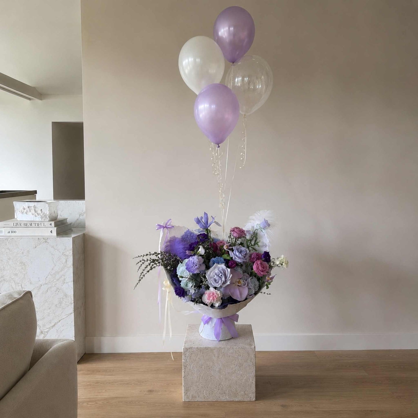Floral arrangement with balloons on a pedestal in a room.