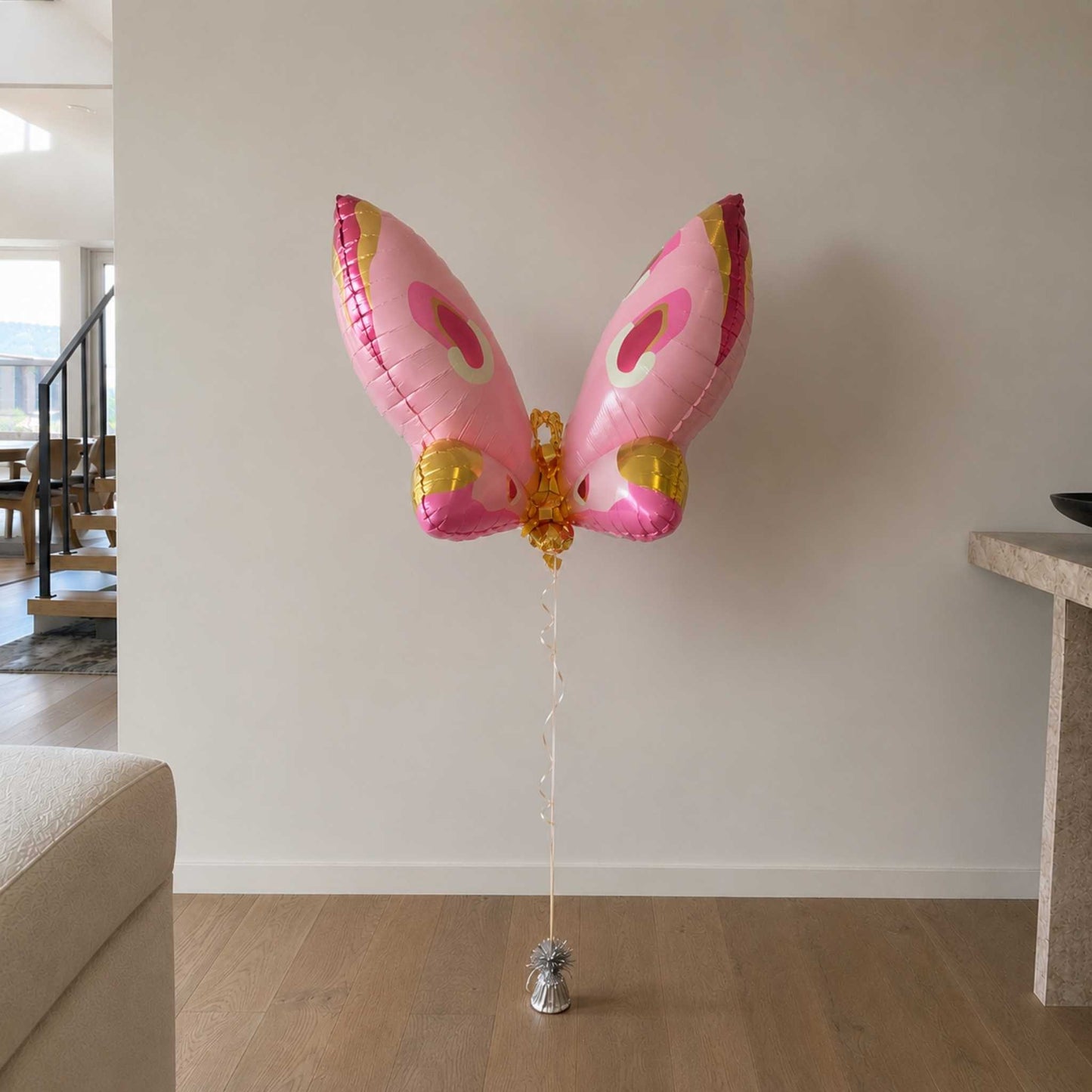 Pink butterfly-shaped balloon on a wooden floor against a white wall.