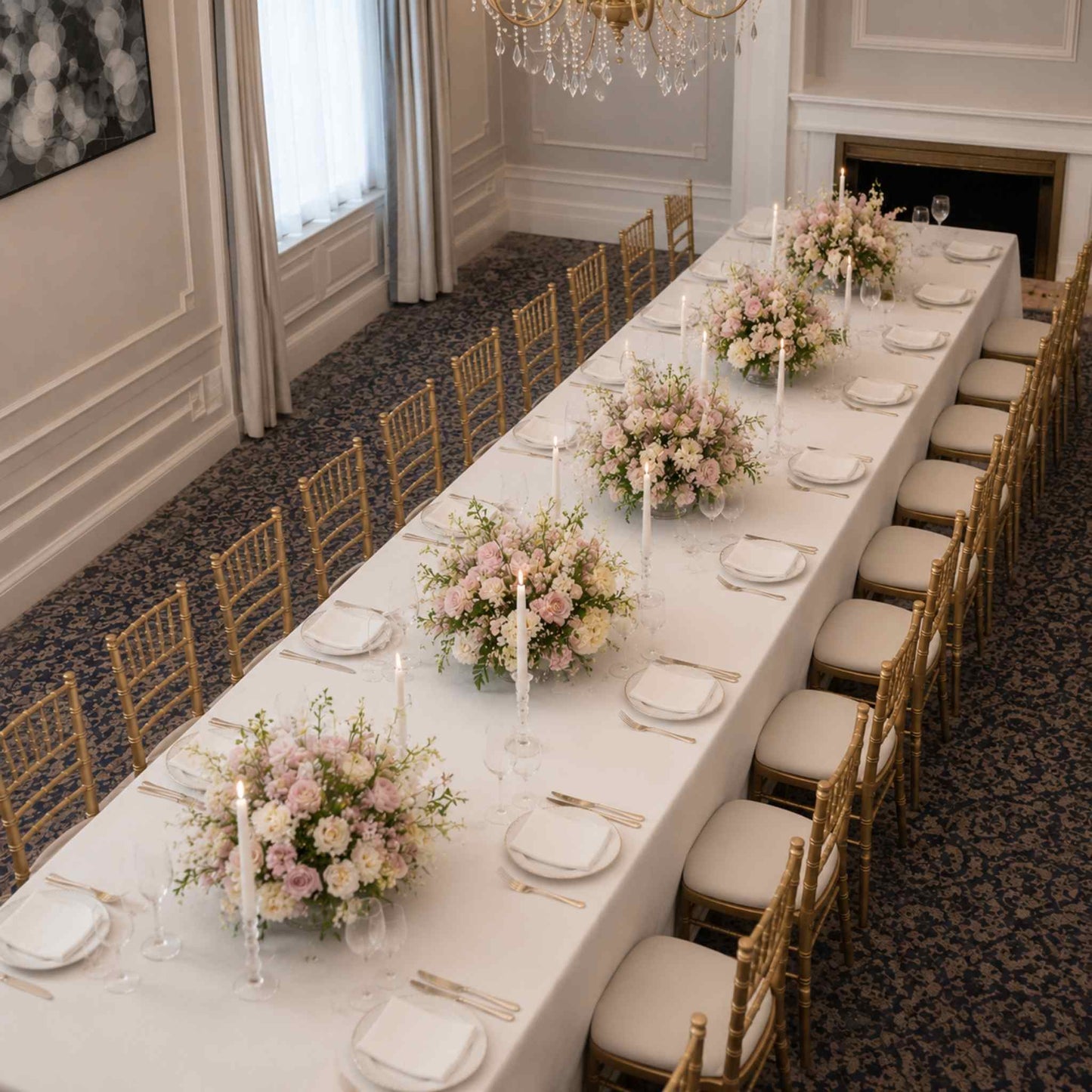 Elegant dining room with a long table set for a formal event, featuring floral centerpieces and gold chairs.
