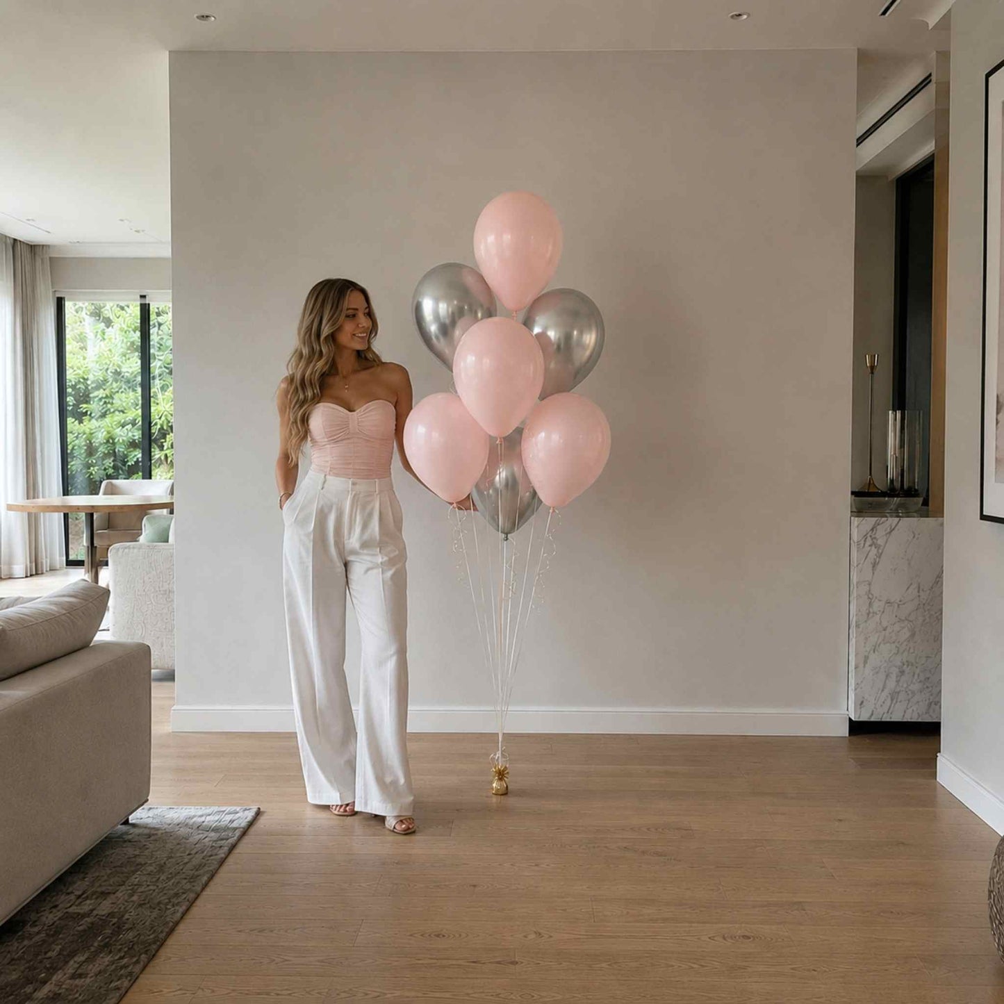 Woman holding pink and silver balloons in a modern living room.