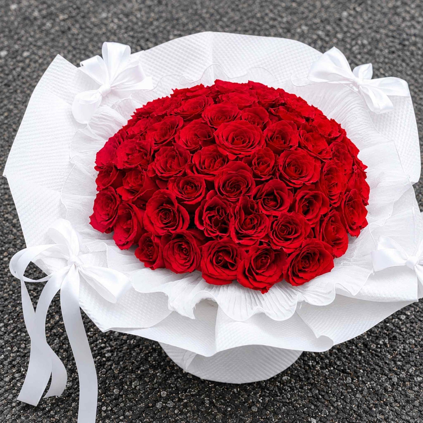 Heart-shaped bouquet of red roses wrapped in white paper on a dark surface