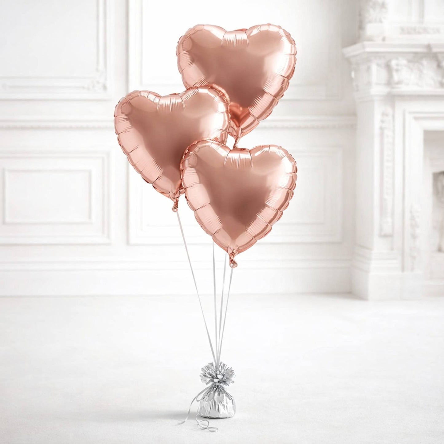 Three rose gold heart-shaped balloons tied together against a white wall.