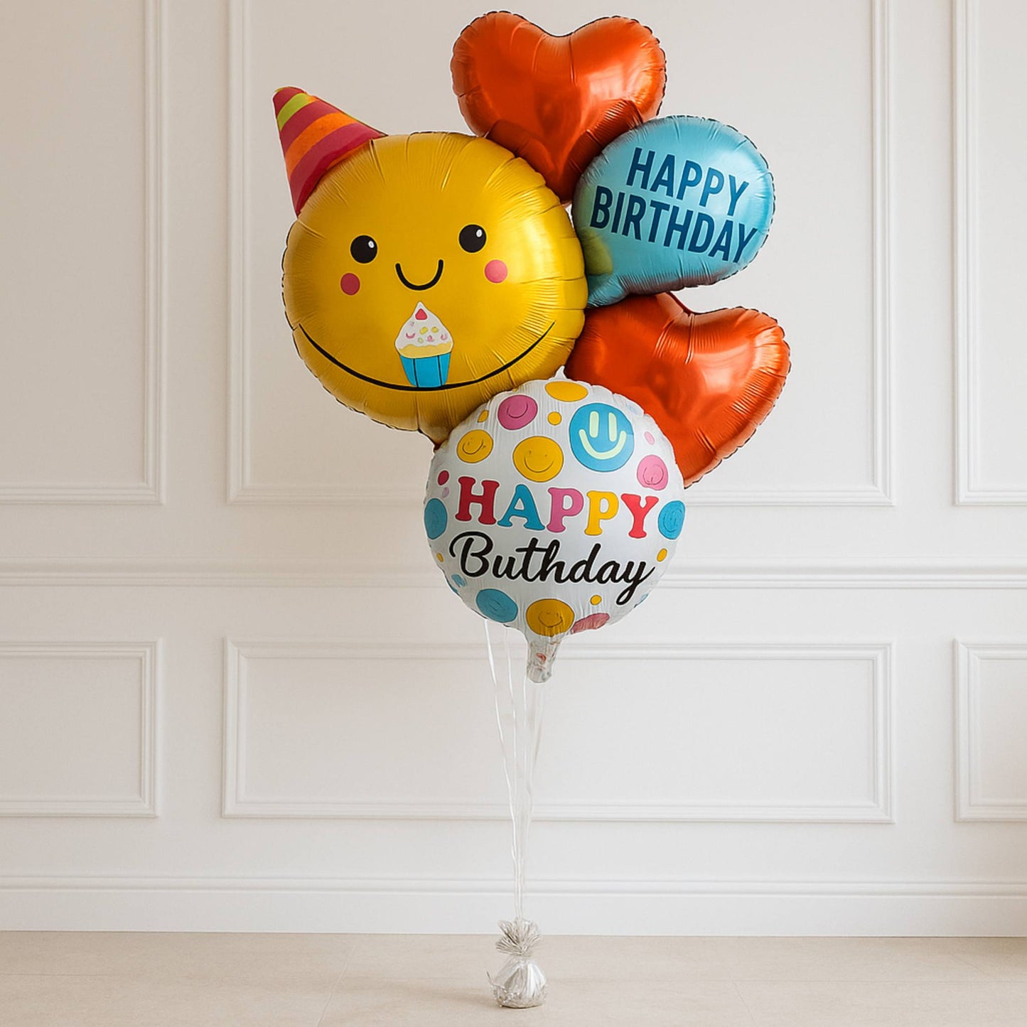 Colorful birthday balloons with smiley face and 'Happy Birthday' text against a white paneled wall.