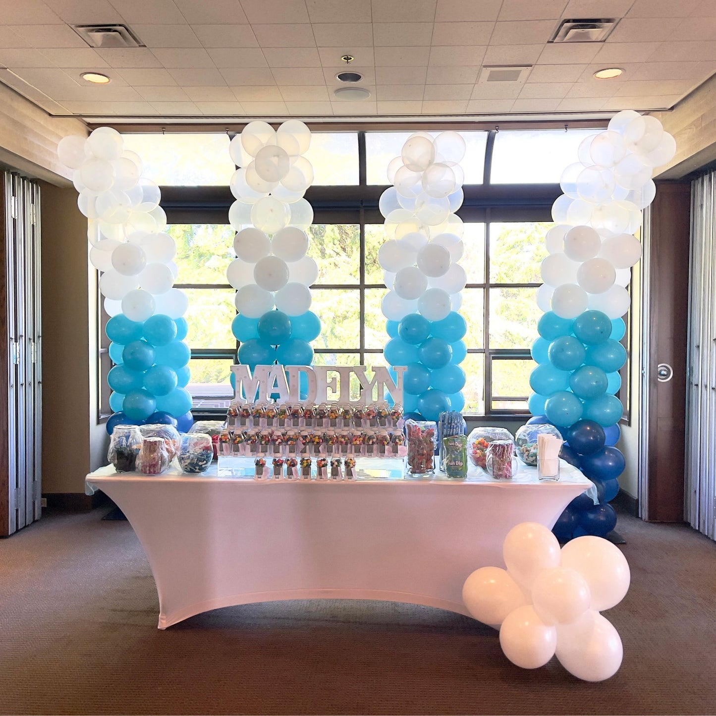 A set of four balloon columns arranged alongside a table at an event, transitioning in color from white to various shades of blue.