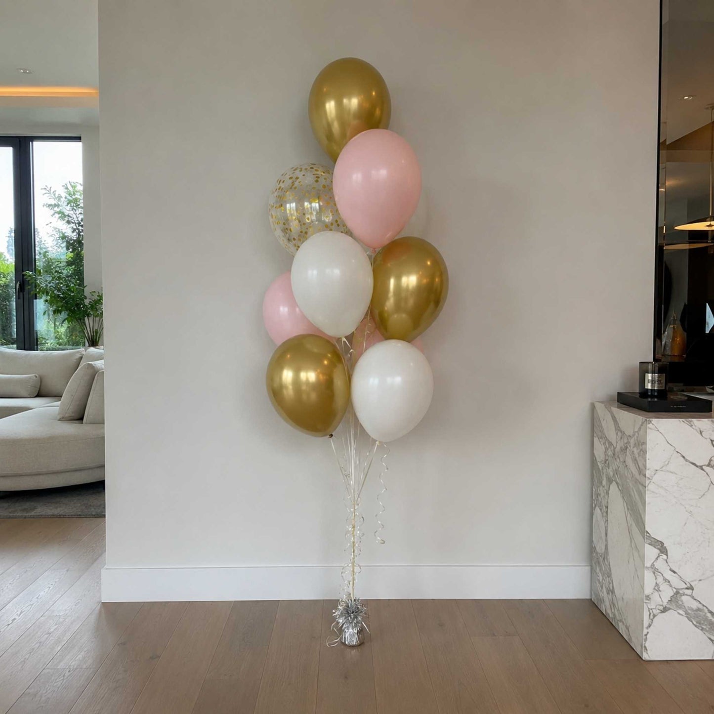 Bouquet of balloons in gold, pink, and white against a white wall in a living room.