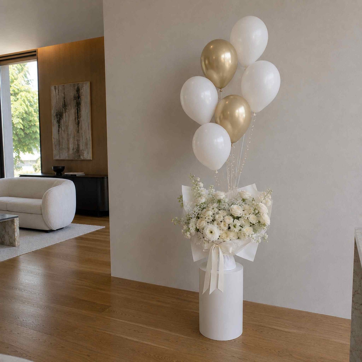 Floral arrangement in a white vase with gold and white balloons in a modern living room.