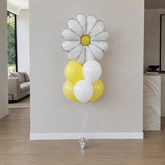 Balloon bouquet shaped like a daisy with white flowers and yellow centers on a plain wall.