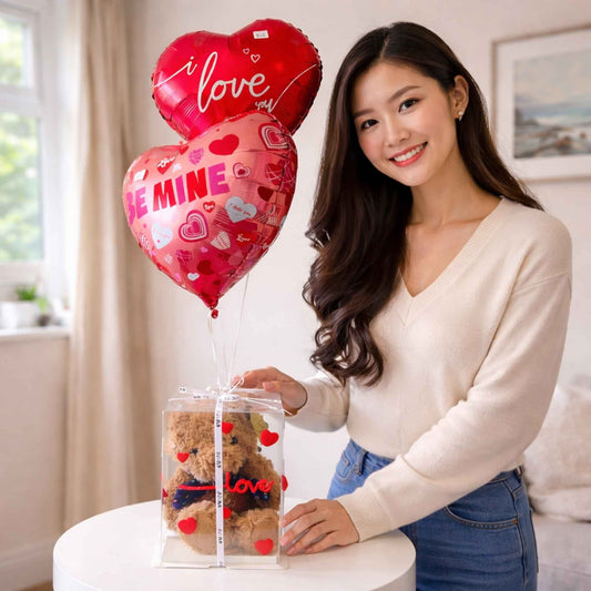 Woman holding a transparent box with a teddy bear and heart-shaped balloons indoors.