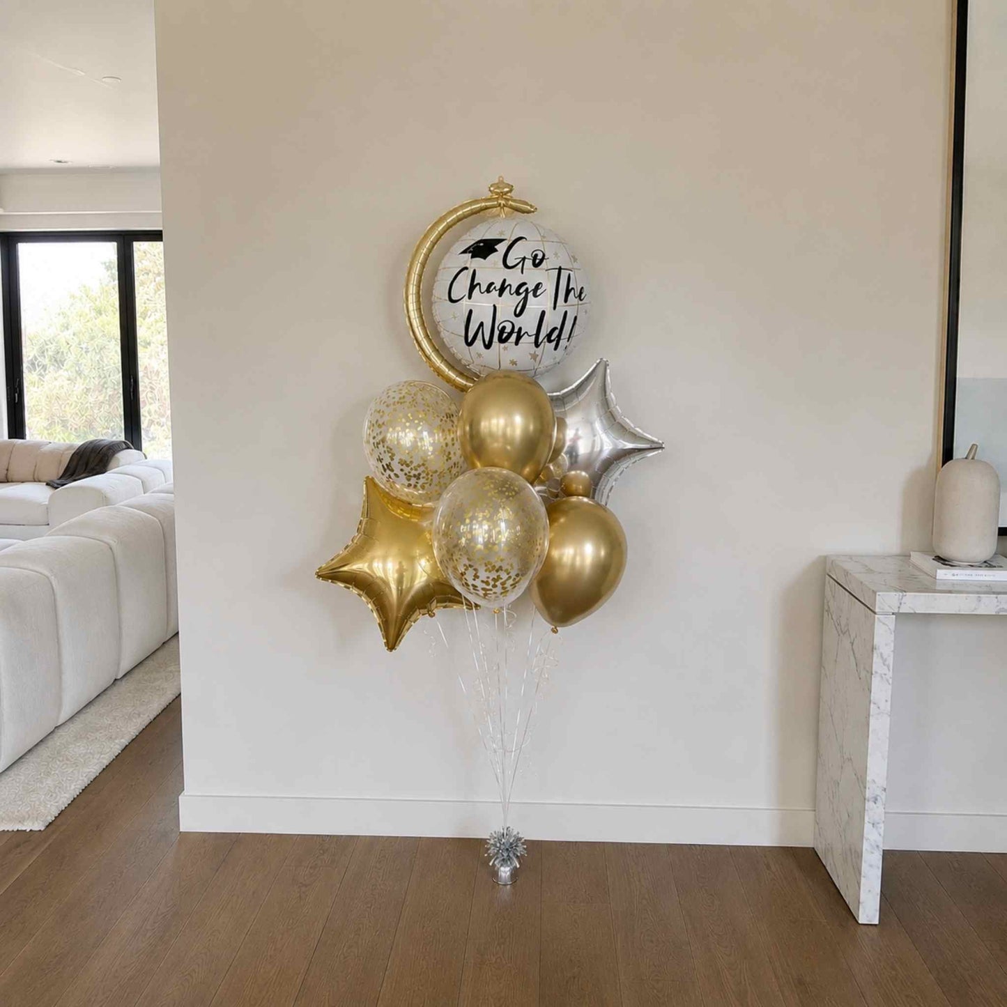 Decorative balloon bouquet with gold and silver balloons against a white wall in a living room.