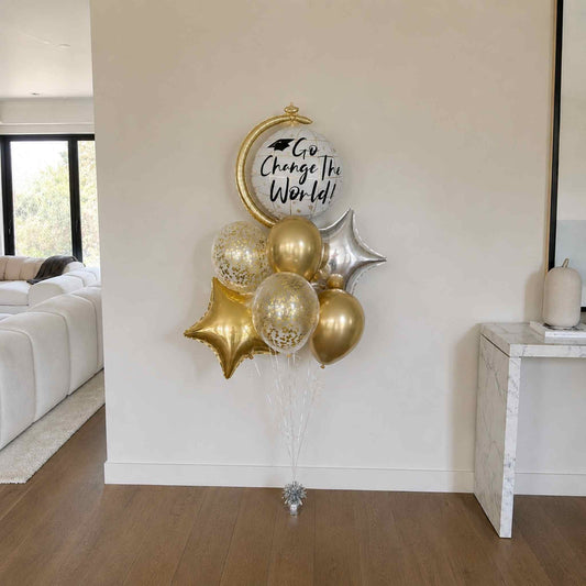 Decorative balloon bouquet with gold and silver balloons against a white wall in a living room.