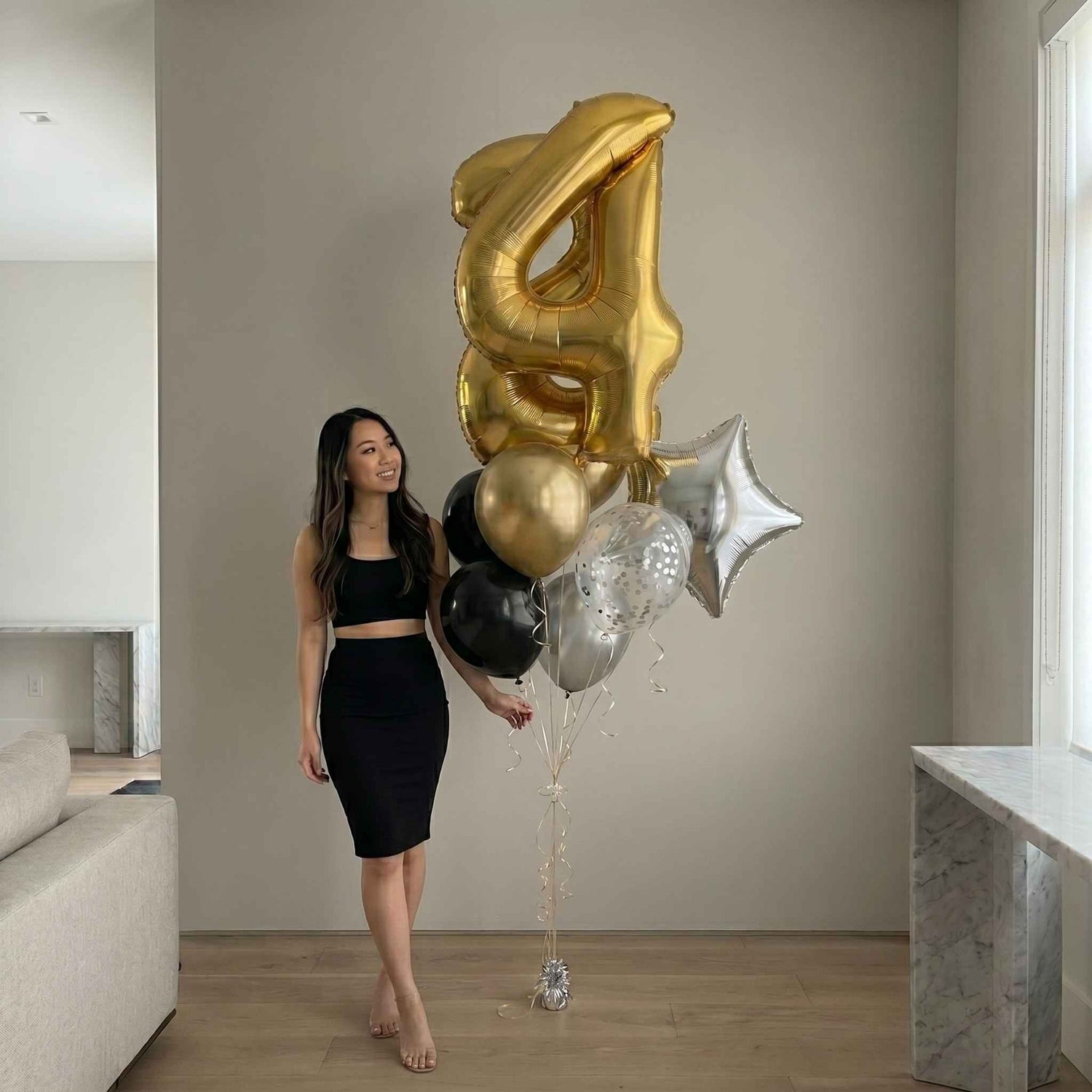 woman sitting by a rose gold balloon bouquet large window view