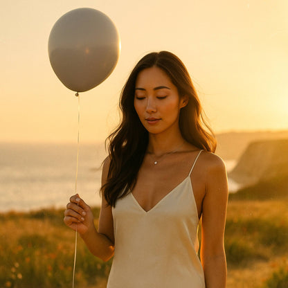 Woman holding a black balloon against a sunset backdrop