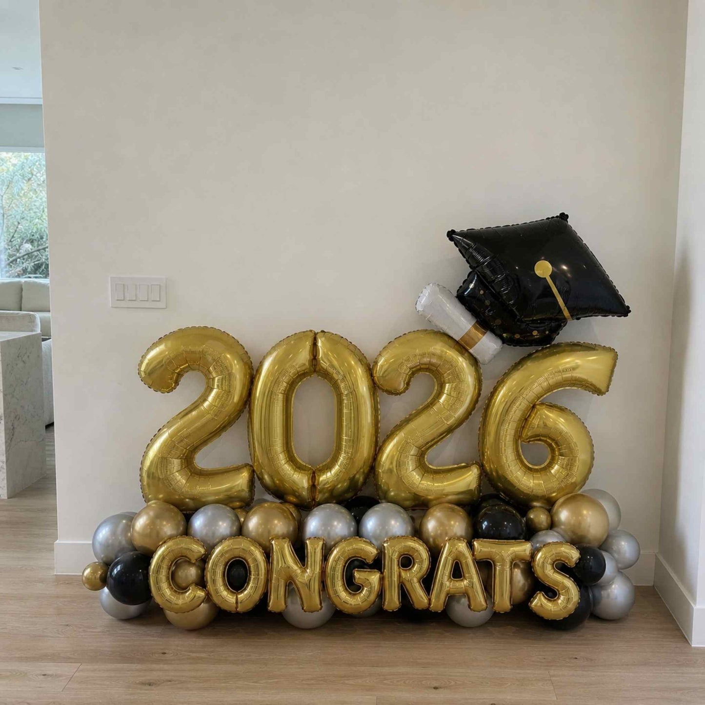 Gold '2026 Congrats' balloons with a graduation cap balloon on a wooden floor.