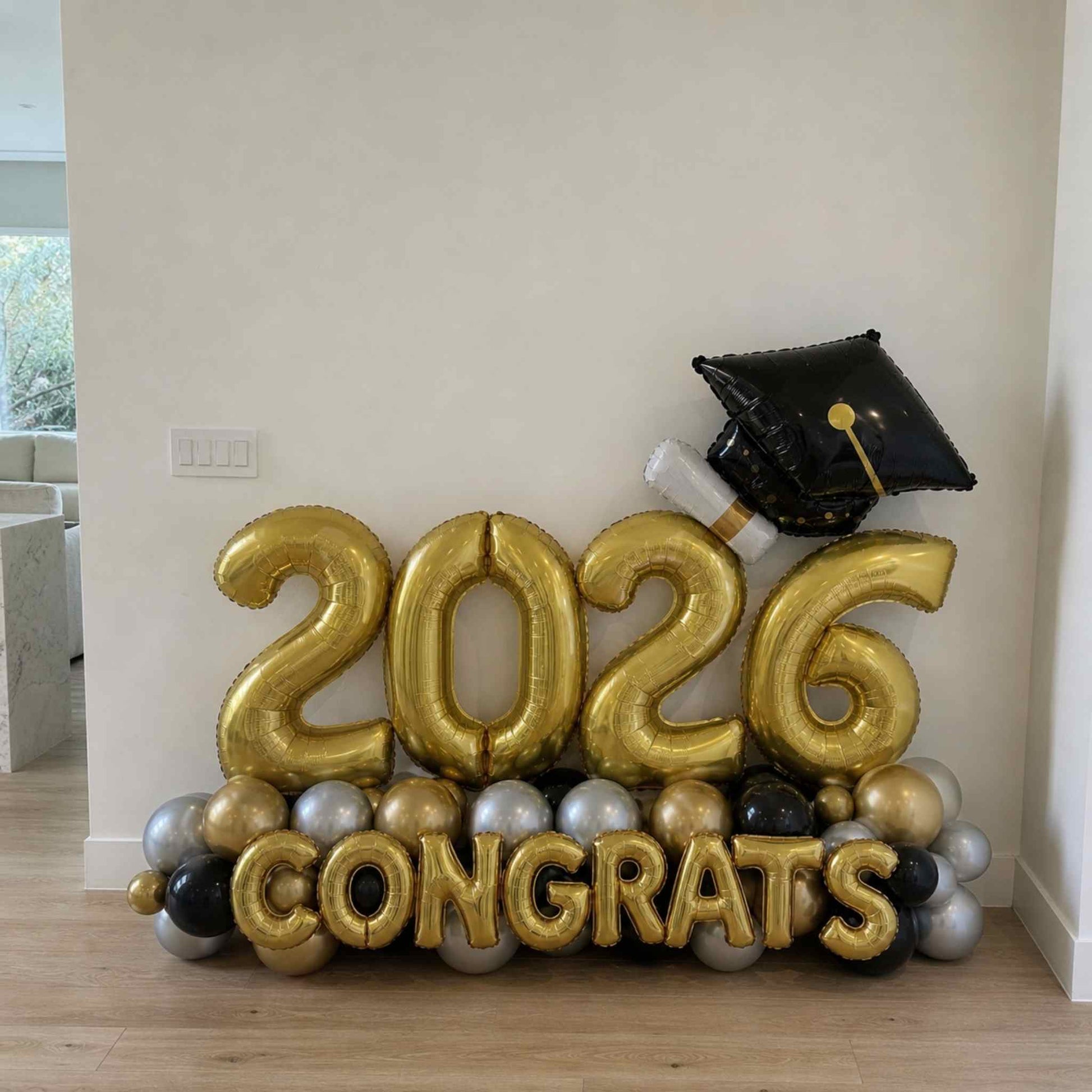 Gold '2026 Congrats' balloons with a graduation cap balloon on a wooden floor.