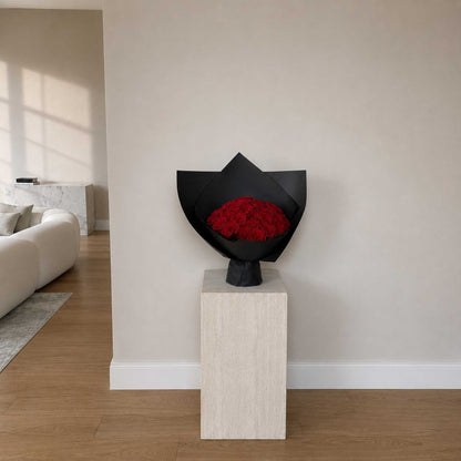 Bouquet of red roses in a black wrap on a white pedestal in a living room.